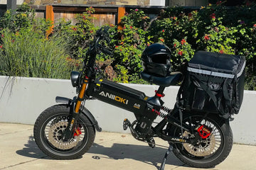 Black Aniioki A8 Pro Max heavy-duty fat tire electric bike parked on a sunny sidewalk, equipped with a delivery backpack on the rear rack and a helmet on the seat