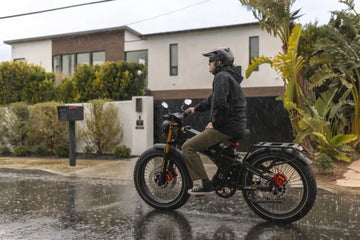 Can you ride electric bike in the rain? A Black electric bike with Asian rider in helmet and rain jacket, riding on a wet residential street with houses and mailbox, showing waterproof performance and everyday practicality.